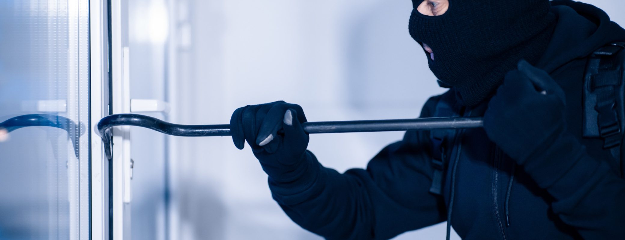 Intrusion Concept. Side view portrait of disguised prowler breaking house or office door with crowbar